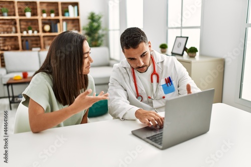 Doctor explain treatment to latin woman using laptop at clinic.