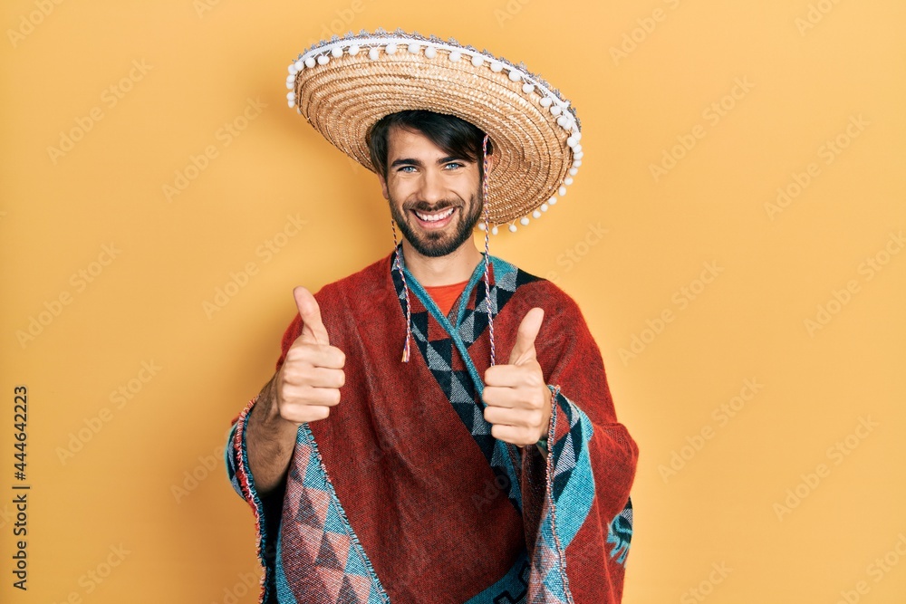 Young hispanic man holding mexican hat approving doing positive gesture