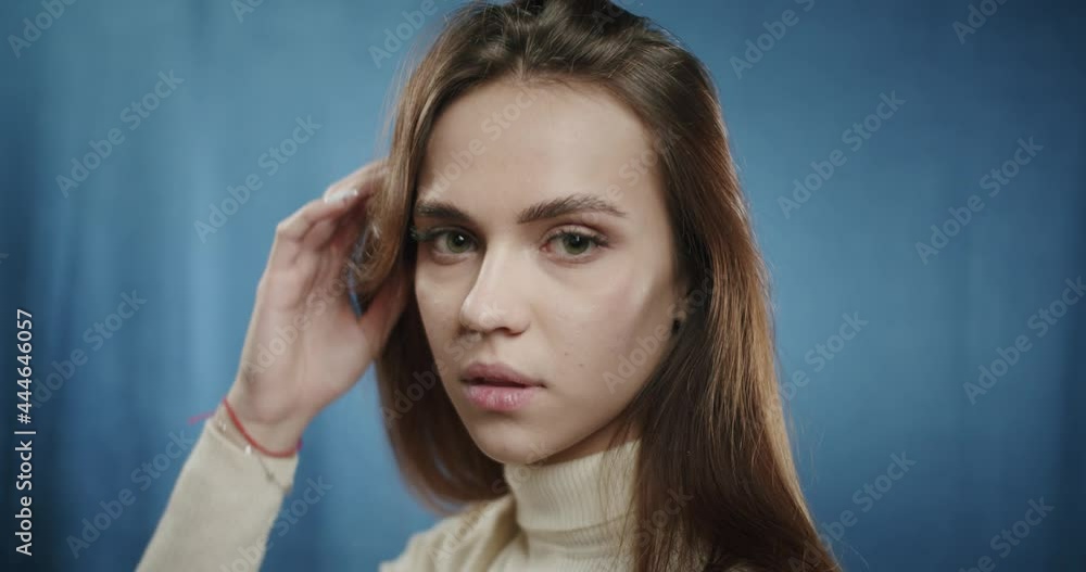 Portrait of beautiful teenager touching her hair, posing in fashion studio on blue background. Close-up of young cute woman smiling, making funny faces, model making positive grimaces. Portrait of beautiful teenager touching her hair, posing in fashion studio on blue background. Close-up of young cute woman smiling, making funny faces, model making positive grimaces.