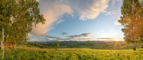 Summer evening, meadows, hills and forest. Sunset light and picturesque sky.