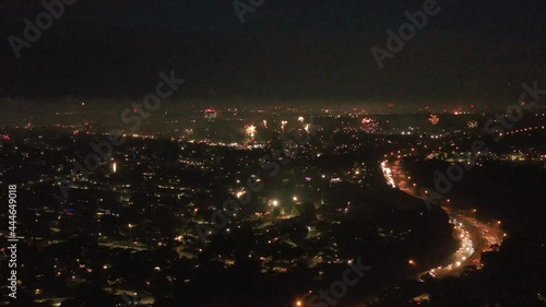 An aerial view of the 2021 4th of July fireworks on Long Island, NY. The drone camera trucks right near a highway, high over the neighborhood as the fireworks go off on the horizon in the darkness.