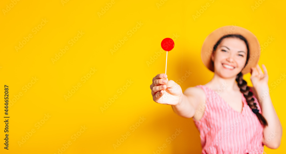 Charming girl in a straw hat holding a lollipop in the shape of a circle on a colorful isolated yellow background Charming girl in a straw hat holding a lollipop in the shape of a circle on a colorful isolated yellow background