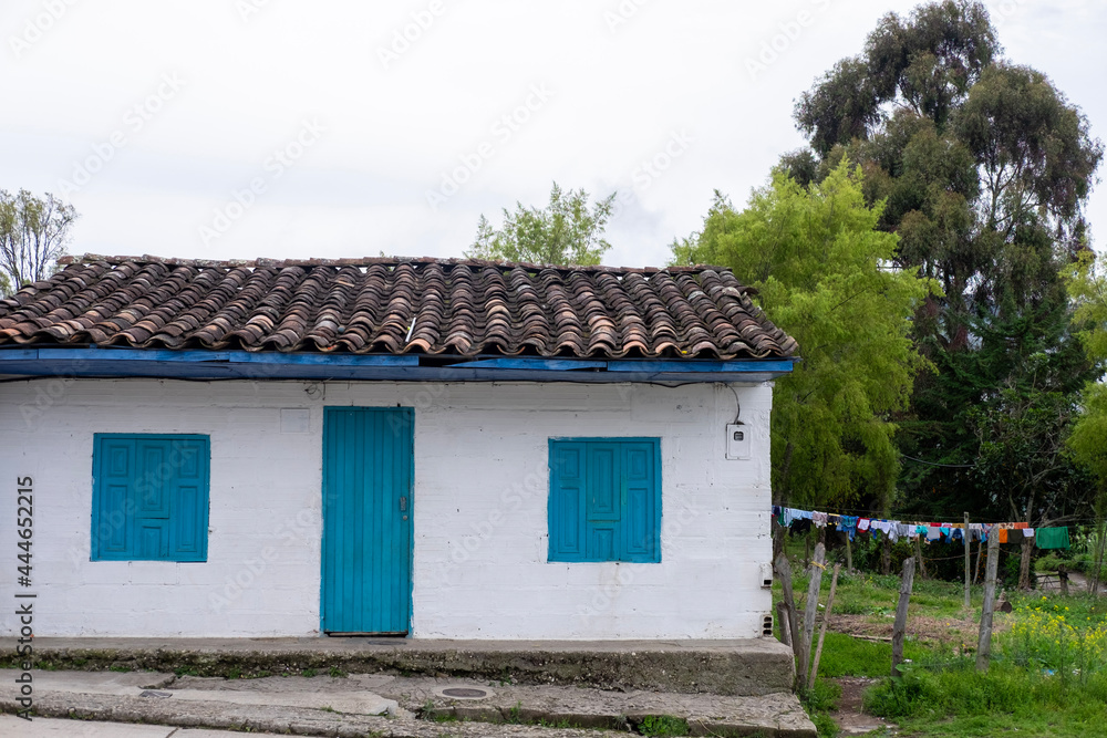 white peasant house with blue wooden doors and windows, and clothes hanging on a rope.