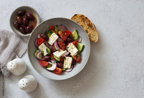 Greek salad with tomatoes, cucumbers, feta cheese and olives in a bowl on gray stone background