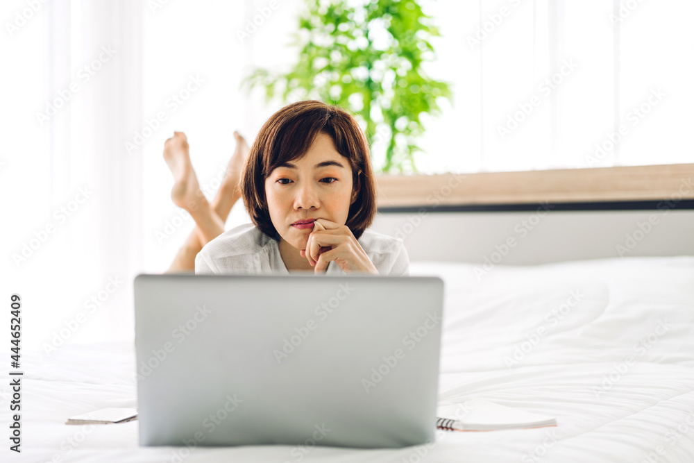 Young smiling happy beautiful asian woman relaxing using laptop computer in the bedroom at home.Young creative girl working and typing on keyboard.work from home concept Young smiling happy beautiful asian woman relaxing using laptop computer in the bedroom at home.Young creative girl working and typing on keyboard.work from home concept