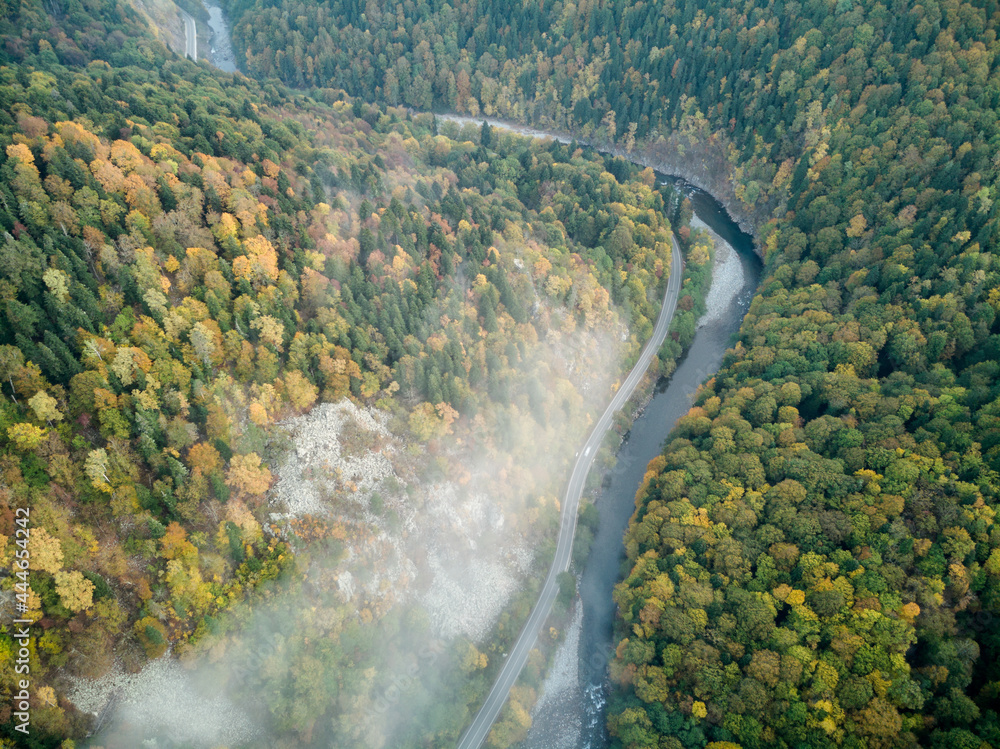 Aerial view of the road and colorful autumn forest with a mountain river in Russia, Adygea