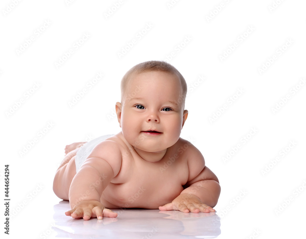 Playful infant child baby girl kid in diaper is lying on her tummy, stomach trying to reach, touch camera, slapping on floor isolated on a white background Playful infant child baby girl kid in diaper is lying on her tummy, stomach trying to reach, touch camera, slapping on floor isolated on a white background