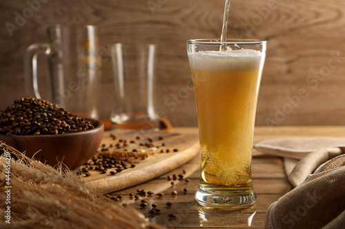Pouring Beer in the beer glass and malt on wooden table background. Alcohol drink concept.