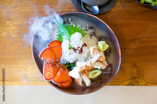 Live Canadian Lobster sashimi on brown ceramic plate with a smoke of dry ice. Served two ways fresh and boiled decorate with fresh wasabi, shredded radish and green shiso leaf. Japanese food, Topview.