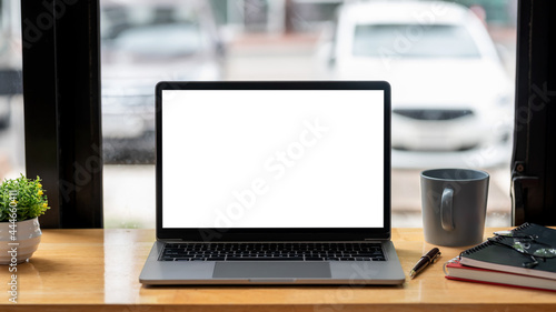 Fototapeta Naklejka Na Ścianę i Meble -  Image of a laptop blank white screen on a desk near a window at the office with a coffee mug.