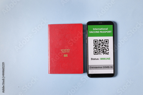 Digital international vaccine passport smart phone screen qr code app coronavirus covid 19 immunization red passport book on light sky blue background