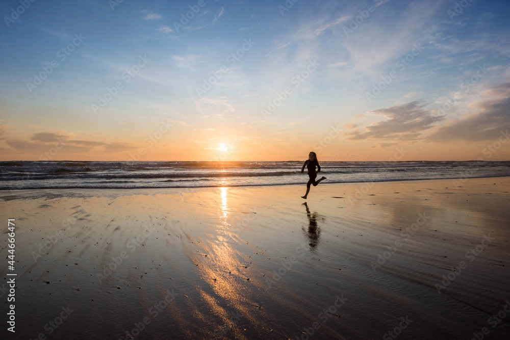 young girl running and jumping with happiness on the beach at sunset