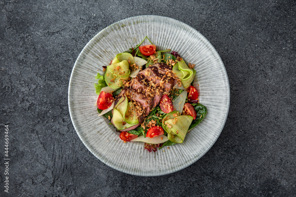 Hearty salad with duck fillet, tomatoes, zucchini and spinach. Diet food. Ready menu for the restaurant. Neutral gray blue textured background Hearty salad with duck fillet, tomatoes, zucchini and spinach. Diet food. Ready menu for the restaurant. Neutral gray blue textured background