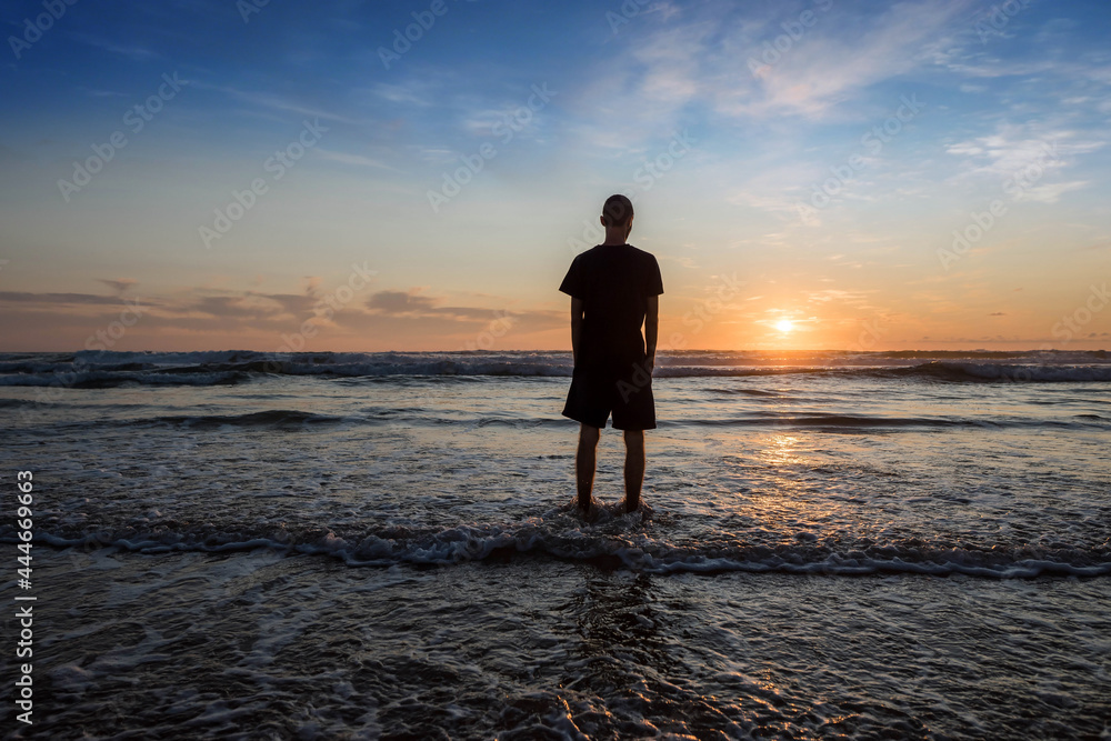 young man walking with feet in water on the beach at sunset