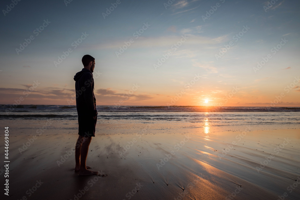 young man walking with feet in water on the beach at sunset