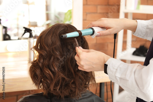 Female hairdresser curling hair of client in beauty salon