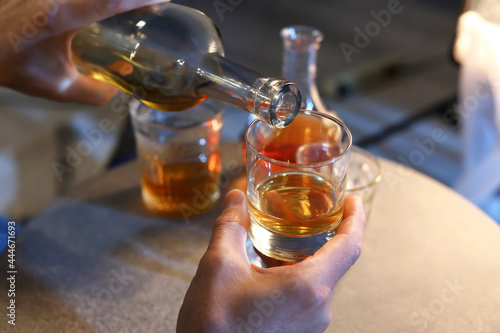 Senior man pouring drink into glass late in evening at home, closeup