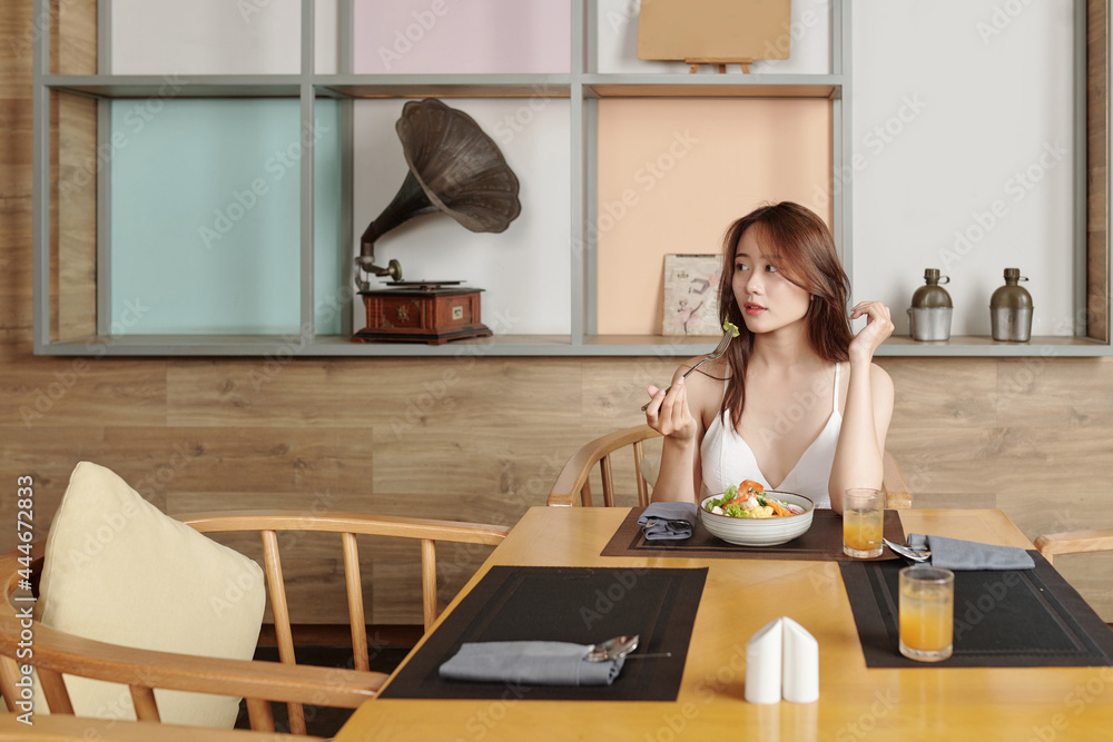 Portrait of beautiful young woman eating lunch at restaurant table alone and looking away Portrait of beautiful young woman eating lunch at restaurant table alone and looking away