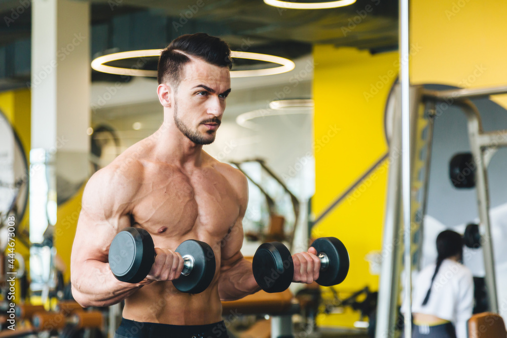 Naklejka premium athletic man doing dumbbell exercise in front of a mirror bare torso in the gym
