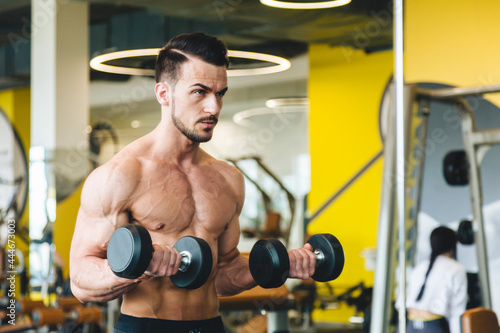 athletic man doing dumbbell exercise in front of a mirror bare torso in the gym