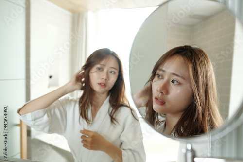 Young woman looking at magnifying mirror when getting ready in bathroom in the morning