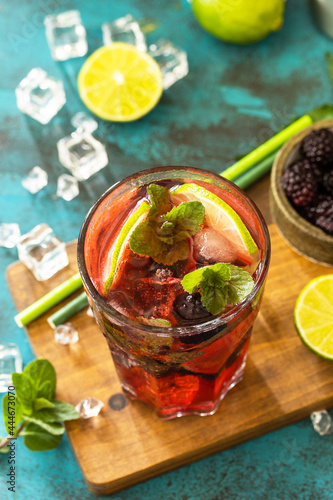Summer refreshing drink with blackberry, mint, lime and ice, mojito or blackberry soda, on a dark stone table.