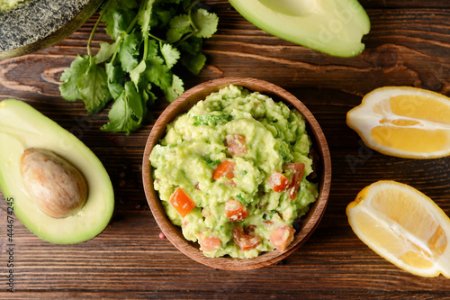 Bowl with tasty guacamole, avocado and lemon on wooden background, closeup