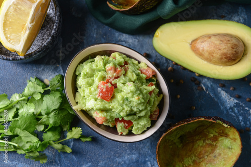 Bowl with tasty guacamole, avocado and lemon on color background