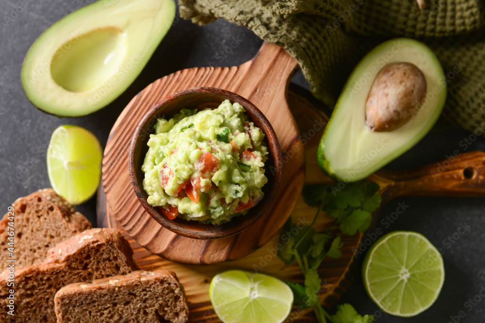 Bowl with tasty guacamole, avocado, lime and bread slices on dark background Bowl with tasty guacamole, avocado, lime and bread slices on dark background