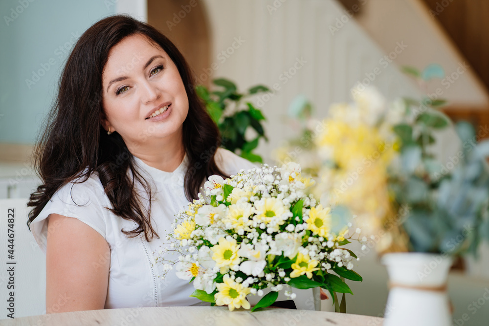 attractive woman in white clothes with flowers at the table in a light room. attractive woman in white clothes with flowers at the table in a light room.