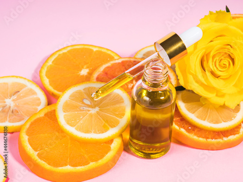 Vitamin C serum bottle with dropper on pink background with orange citrus slices