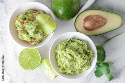 Bowls with tasty guacamole, avocado and lime on light background