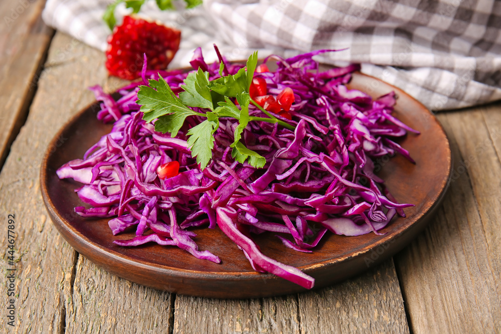 Plate with cut fresh purple cabbage and pomegranate on wooden background, closeup