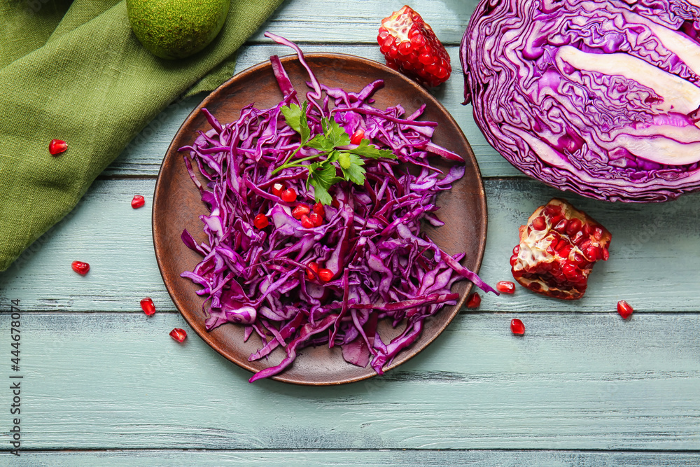 Plate with cut fresh purple cabbage and pomegranate on color wooden background
