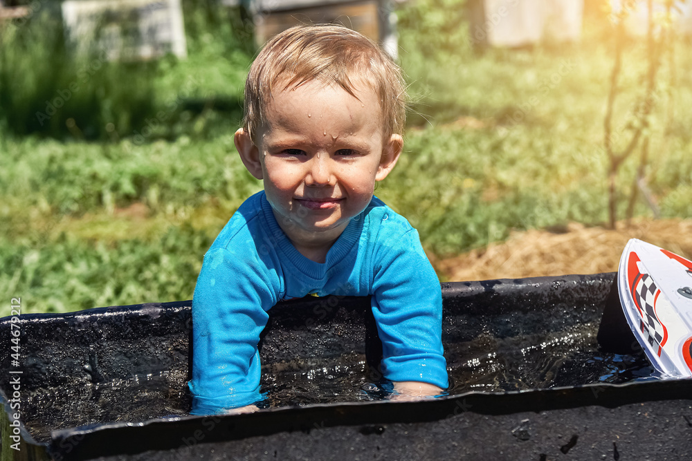 Little wet boy looks at camera and plays with clean water in trough in