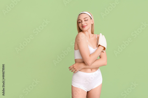 Beautiful young woman with massage mitten on color background