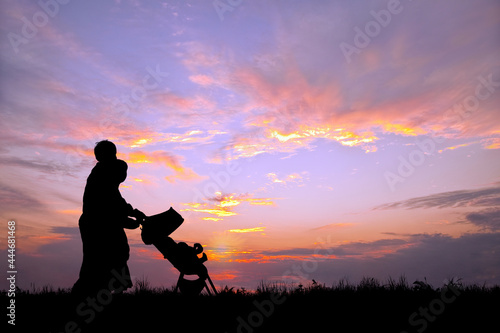 夕日の空を背景にベビーカーを押し散歩をする若い夫婦 © chikala