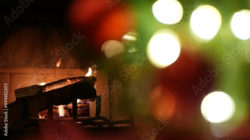 Christmas tree lights by fire in fireplace, New Year or Xmas decoration of pine or fir with red balls. Fireside on winter christmastime holiday. Cozy place by firewood. Seamless looped cinemagraph.