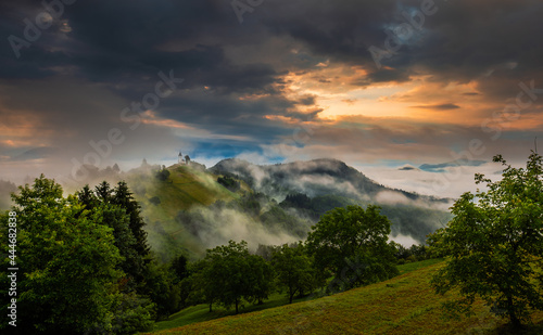 Jamnik, Slovenia - Magical foggy summer sunrise at Jamnik St.Primoz church. The fog gently goes by the small chapel with colorful sky and Julian Alps at background