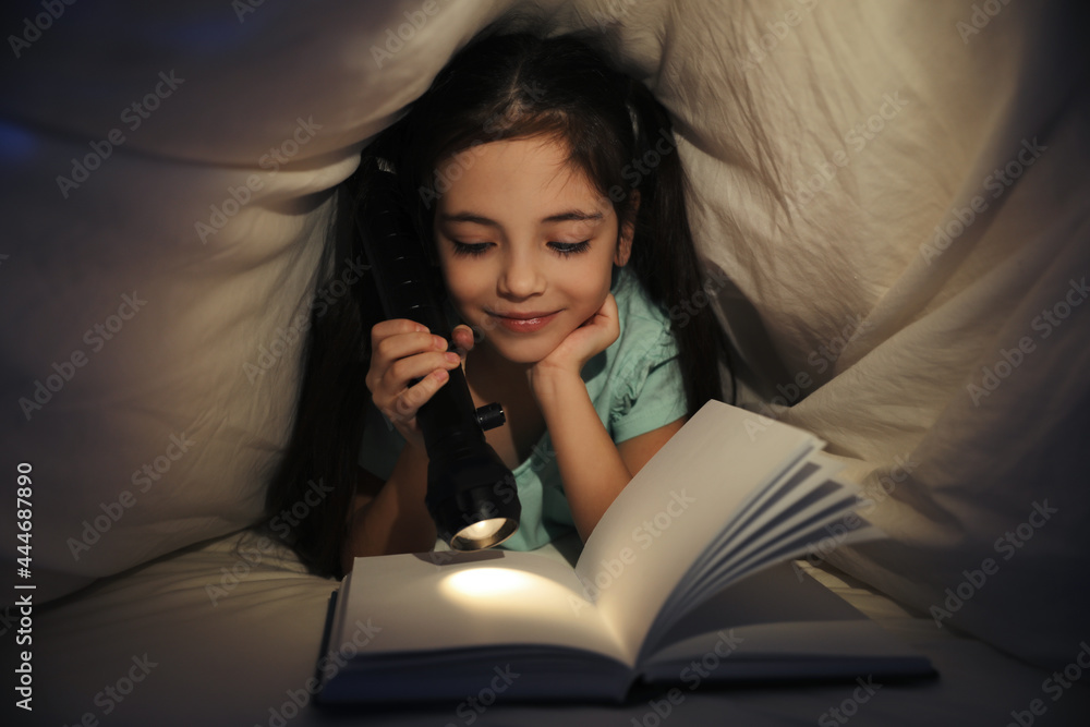 Little girl reading fairy tale under blanket in dark bedroom Little girl reading fairy tale under blanket in dark bedroom