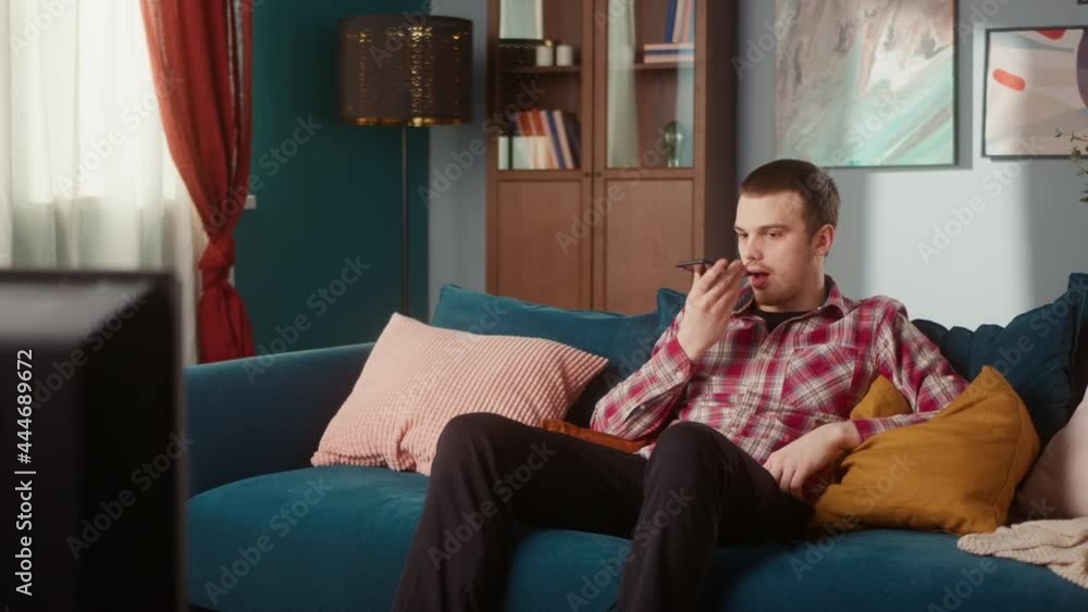 Brutal teenager with a nose piercing and earrings making voice message on smartphone, brown-eyed man sitting on sofa speaking with friends. Communication online during covid lockdown Brutal teenager with a nose piercing and earrings making voice message on smartphone, brown-eyed man sitting on sofa speaking with friends. Communication online during covid lockdown