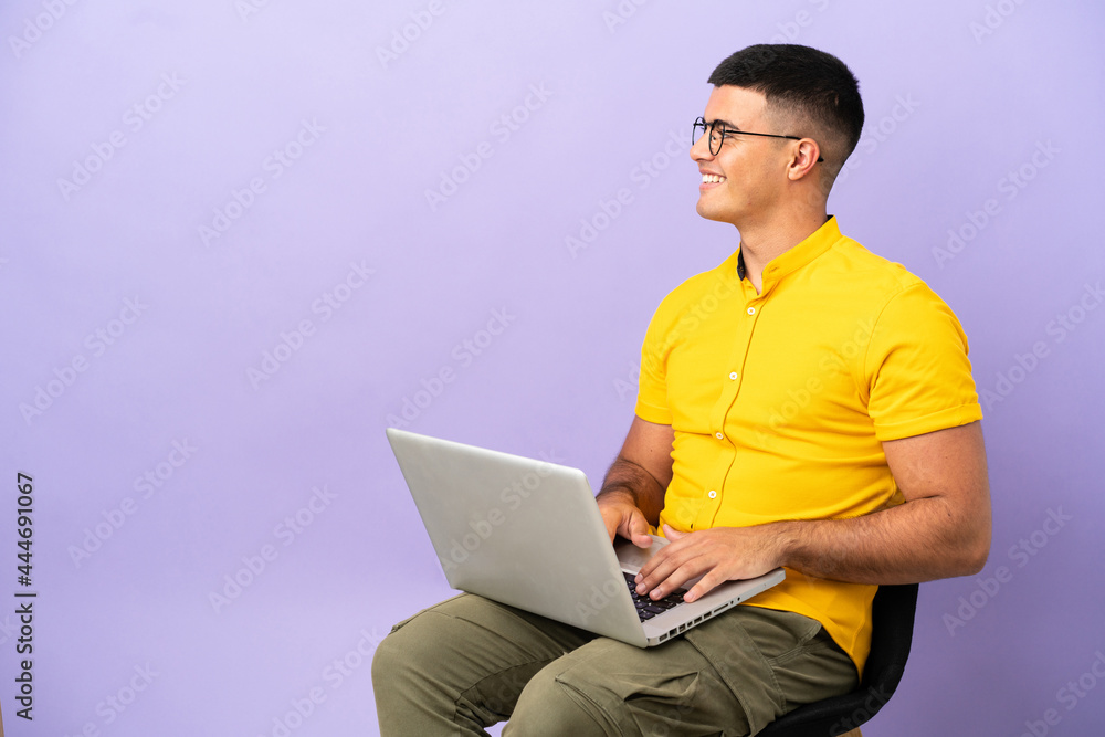 Young man sitting on a chair with laptop looking side Young man sitting on a chair with laptop looking side