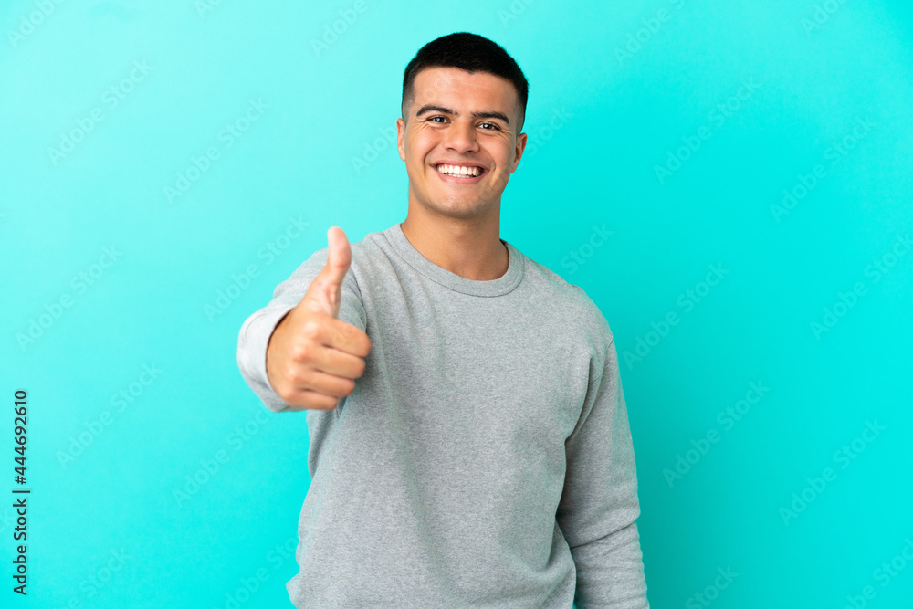 Young handsome man over isolated blue background with thumbs up because something good has happened Young handsome man over isolated blue background with thumbs up because something good has happened