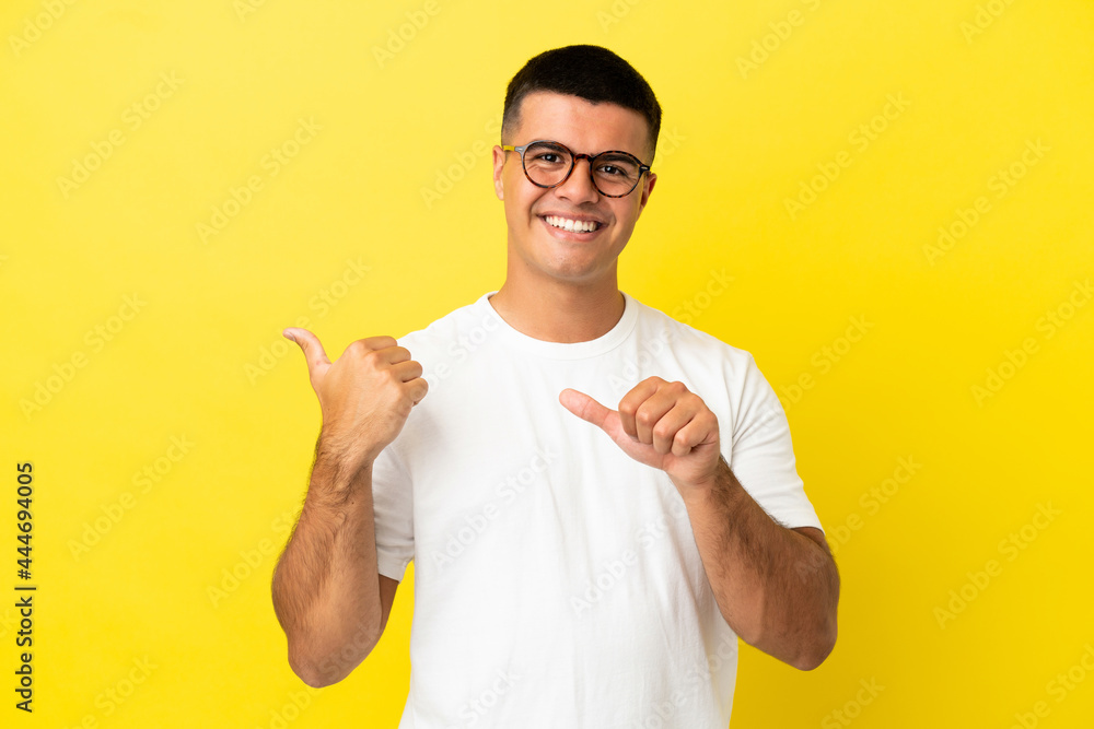 Young handsome man over isolated yellow background pointing to the side to present a product Young handsome man over isolated yellow background pointing to the side to present a product