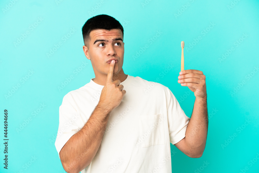 Young handsome man brushing teeth over isolated blue background having doubts while looking up Young handsome man brushing teeth over isolated blue background having doubts while looking up