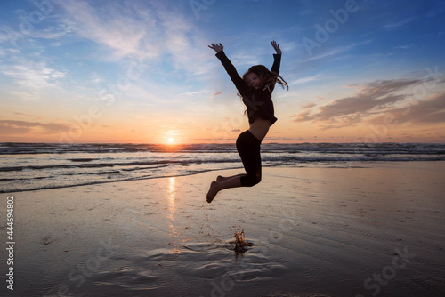 young girl jumping for happiness on the beach at sunset