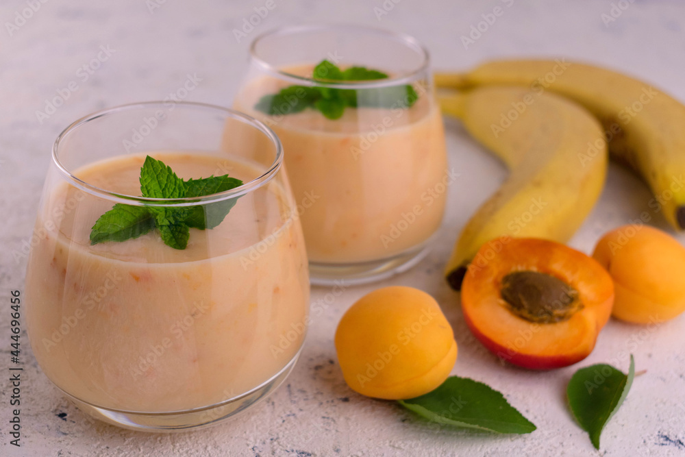 Two glasses with apricot smoothie with banana decorated with a mint leaf on a white background. Two glasses with apricot smoothie with banana decorated with a mint leaf on a white background.