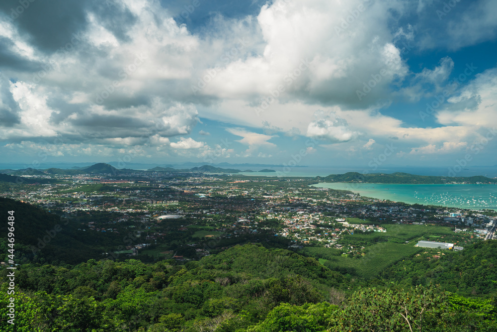 Obraz premium Top view of the city on a tropical island surrounded by green hills and the sea, cloudy weather. Summer vacation and nature travel adventure concept.. Summer composition.