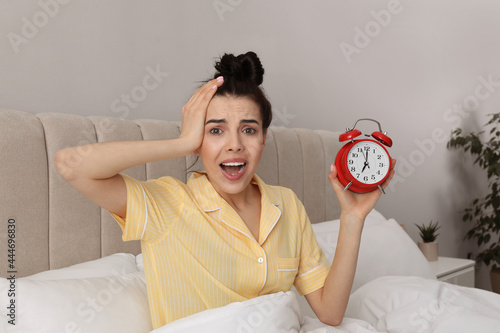 Emotional overslept woman with alarm clock in bed. Being late concept
