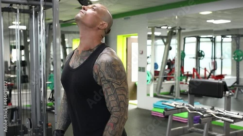 A man with tattoos, with a shaved head, does a warm-up in the gym before a strength training